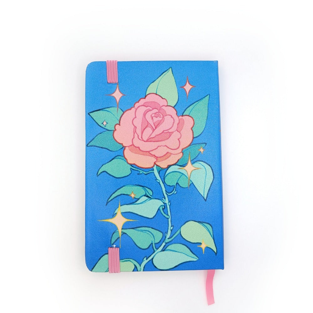 A blue notebook. The notebook has a single pink rose stem with leaves and thorns. There are yellow sparkles surrounding it.  It has a pink elastic.