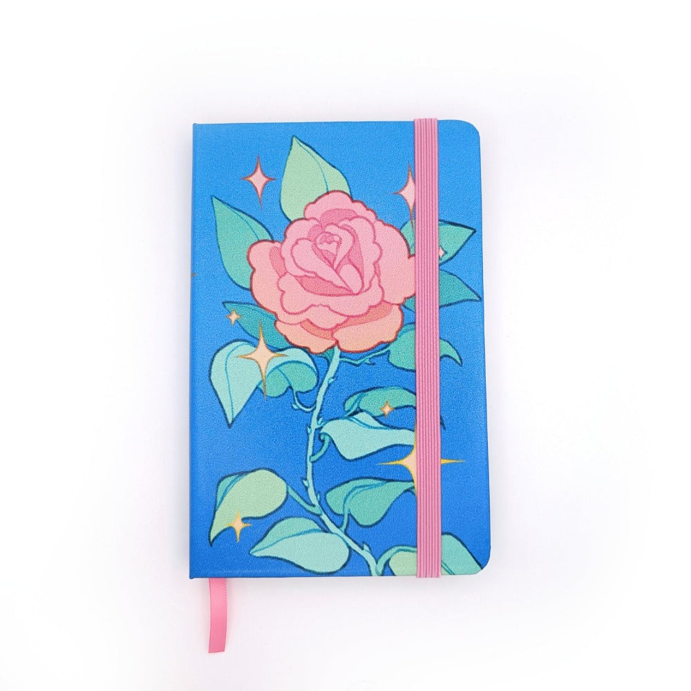 A blue notebook. The notebook has a single pink rose stem with leaves and thorns. There are yellow sparkles surrounding it.  It has a pink elastic.