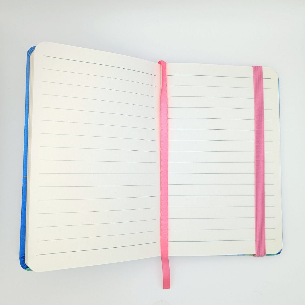 An A6 sized notebook opened up. It has lined paper, a pink bookmark, and pink elastic.