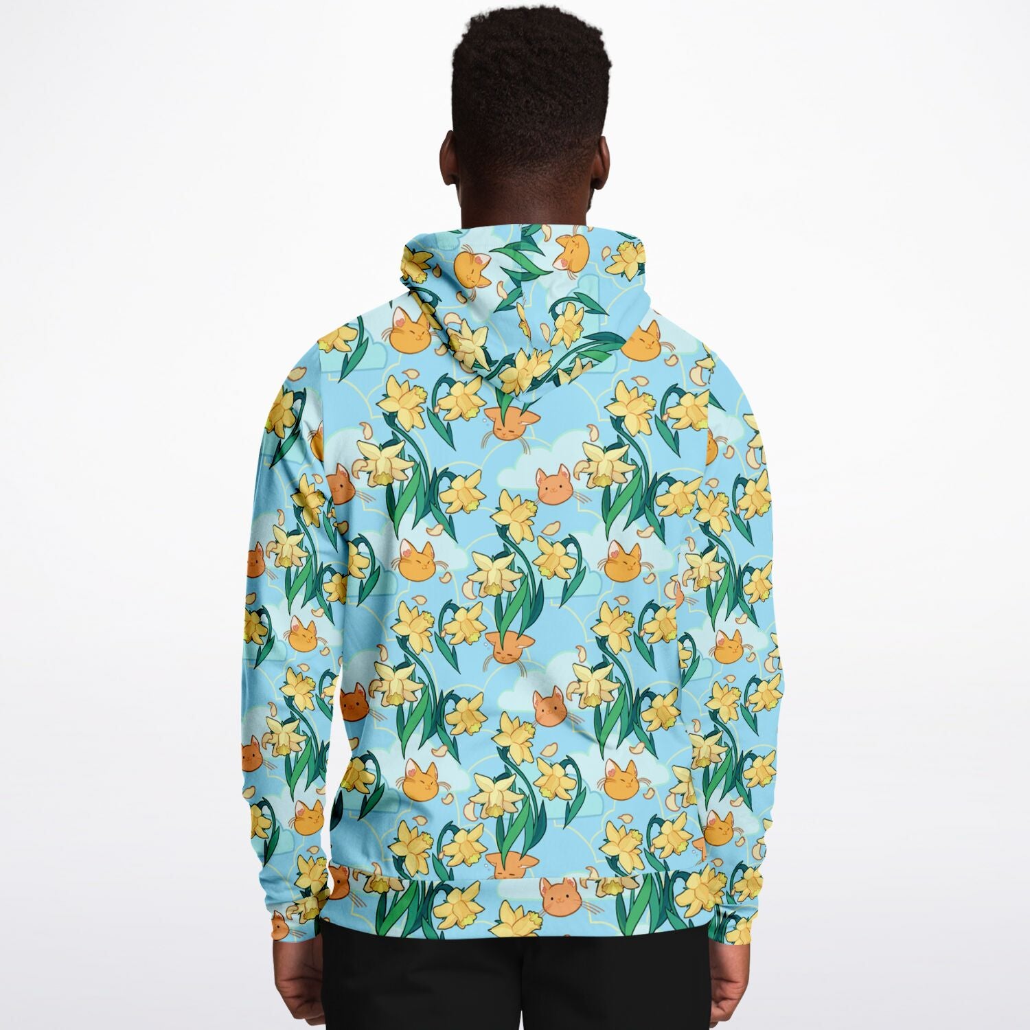 A model wearing a hoodie. The hoodie's pattern features cute cat faces and daffodils on a blue background. The pocket and lining of the hood are orange