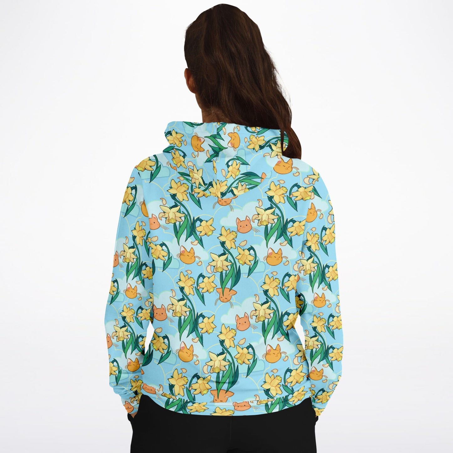 A model wearing a hoodie. The hoodie's pattern features cute cat faces and daffodils on a blue background. The pocket and lining of the hood are orange