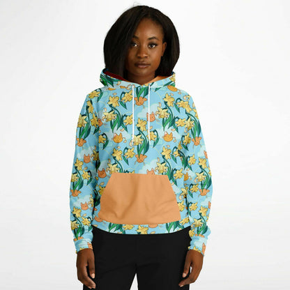 A model wearing a hoodie. The hoodie's pattern features cute cat faces and daffodils on a blue background. The pocket and lining of the hood are orange