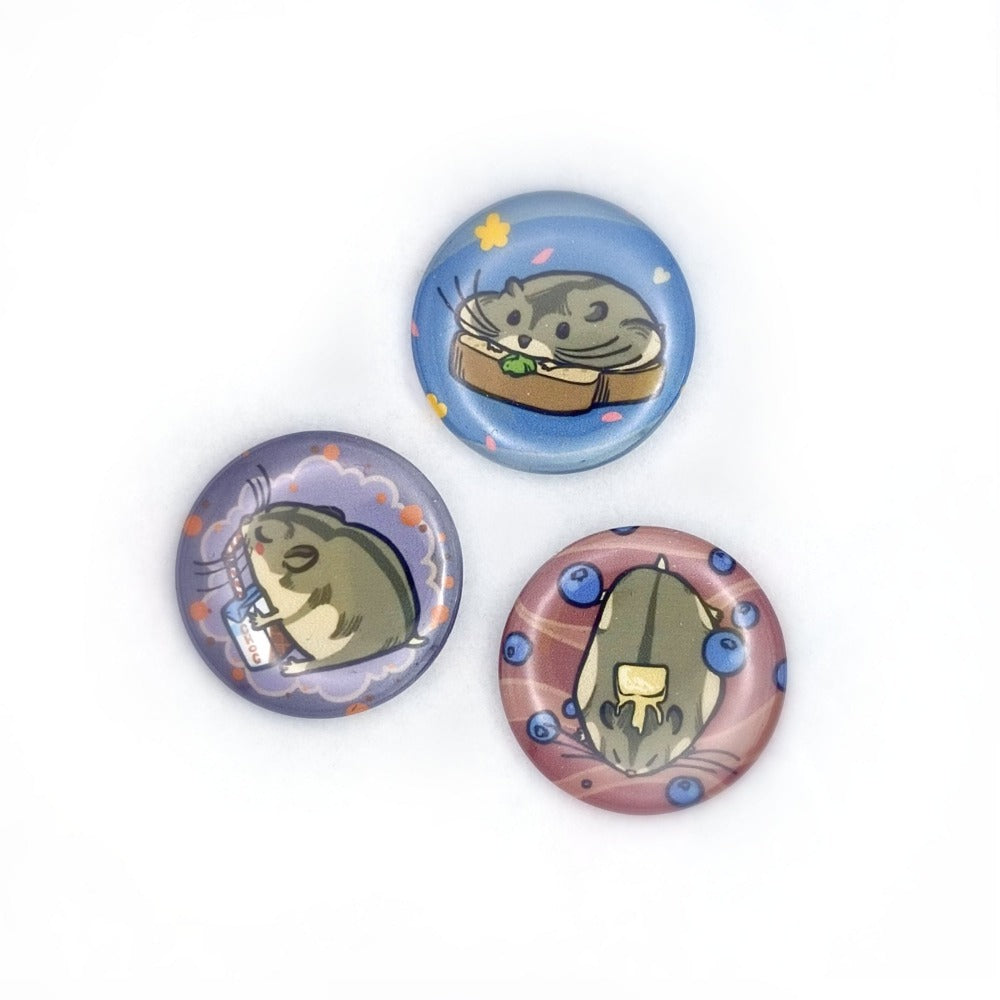 3 small buttons with russian dwarf hamsters. Top is blue with a hamster on top of a sandwich. Left is purple with a hamster drinking chocolate milk. Right is Red, with a hamster surrounded by blueberries and with a piece of melted butter on its head.