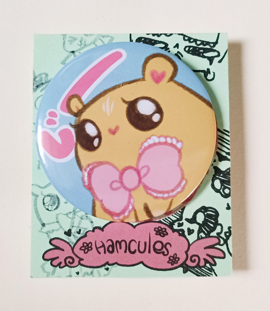 A Large button of a yellow hamster with a big pink bow. It has big sparkly eyes, and hearts for a nose and ears.  The background is light blue and reads the  onomatopoeia "じー" (stare~) in pink.