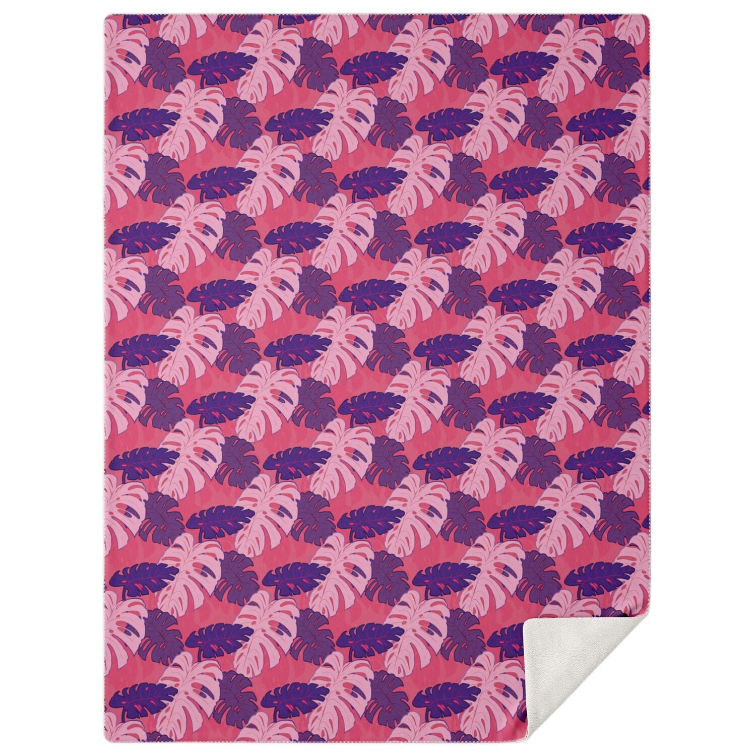 A blanket draped over a couch. The blanket has a monstera pattern with purple and light pink leaves on a pink background.