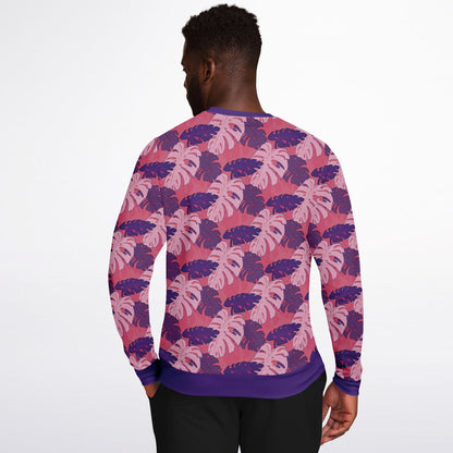 A model wearing a sweatshirt. The sweatshirt's pattern features monstera leaves with purple and light pink leaves on a pink background.