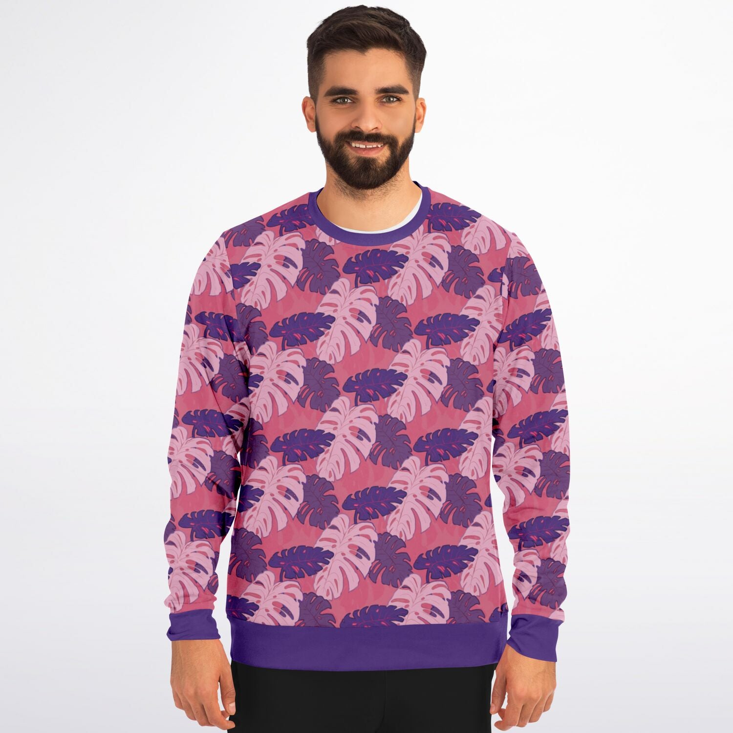 A model wearing a sweatshirt. The sweatshirt's pattern features monstera leaves with purple and light pink leaves on a pink background.