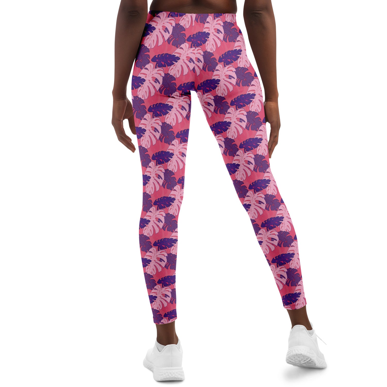 A model wearing leggings. The leggings' pattern features monstera leaves with purple and light pink leaves on a pink background.