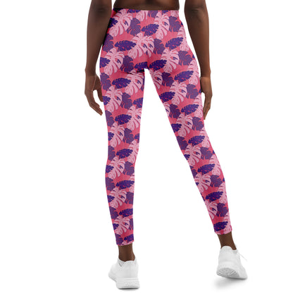 A model wearing leggings. The leggings' pattern features monstera leaves with purple and light pink leaves on a pink background.