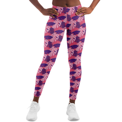 A model wearing leggings. The leggings' pattern features monstera leaves with purple and light pink leaves on a pink background.