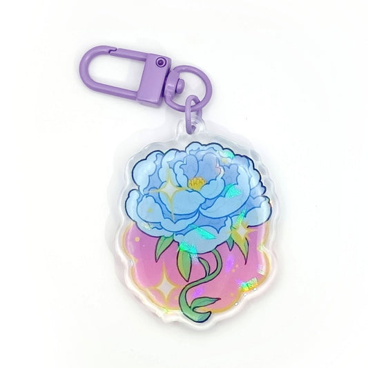 Peony charm. The keychain itself is purple. The charm has a blue Peony on a purple-pink gradient, and is topped off with a holo shard texture.