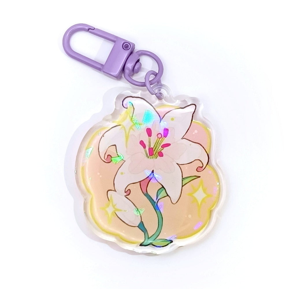 Lily charm. The keychain itself is purple. The charm has a white Lily on an orange-yellow gradient, and is topped off with a holo shard texture.