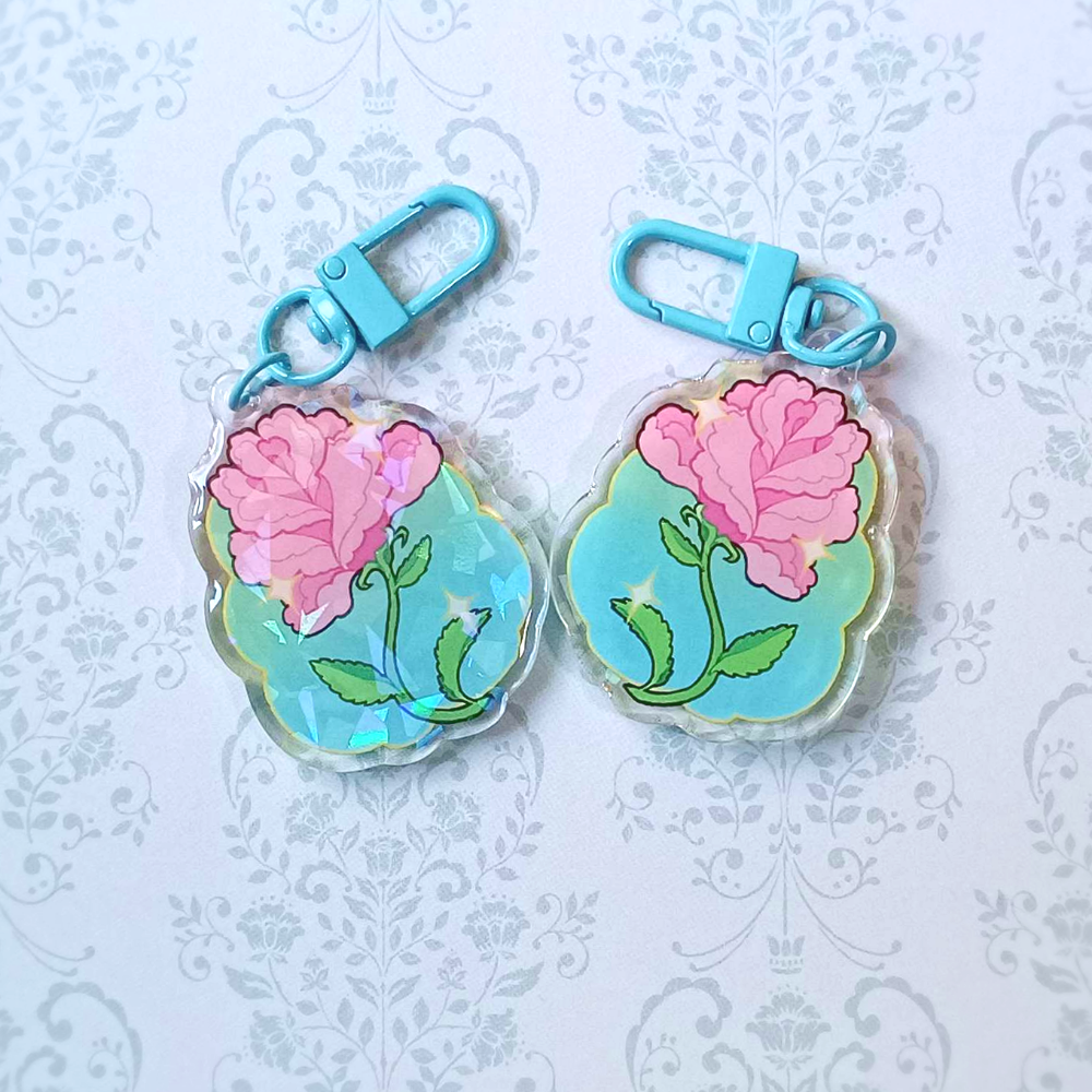 Two rose charms, one showing the frontside with holo and resin, and one showing the backside.