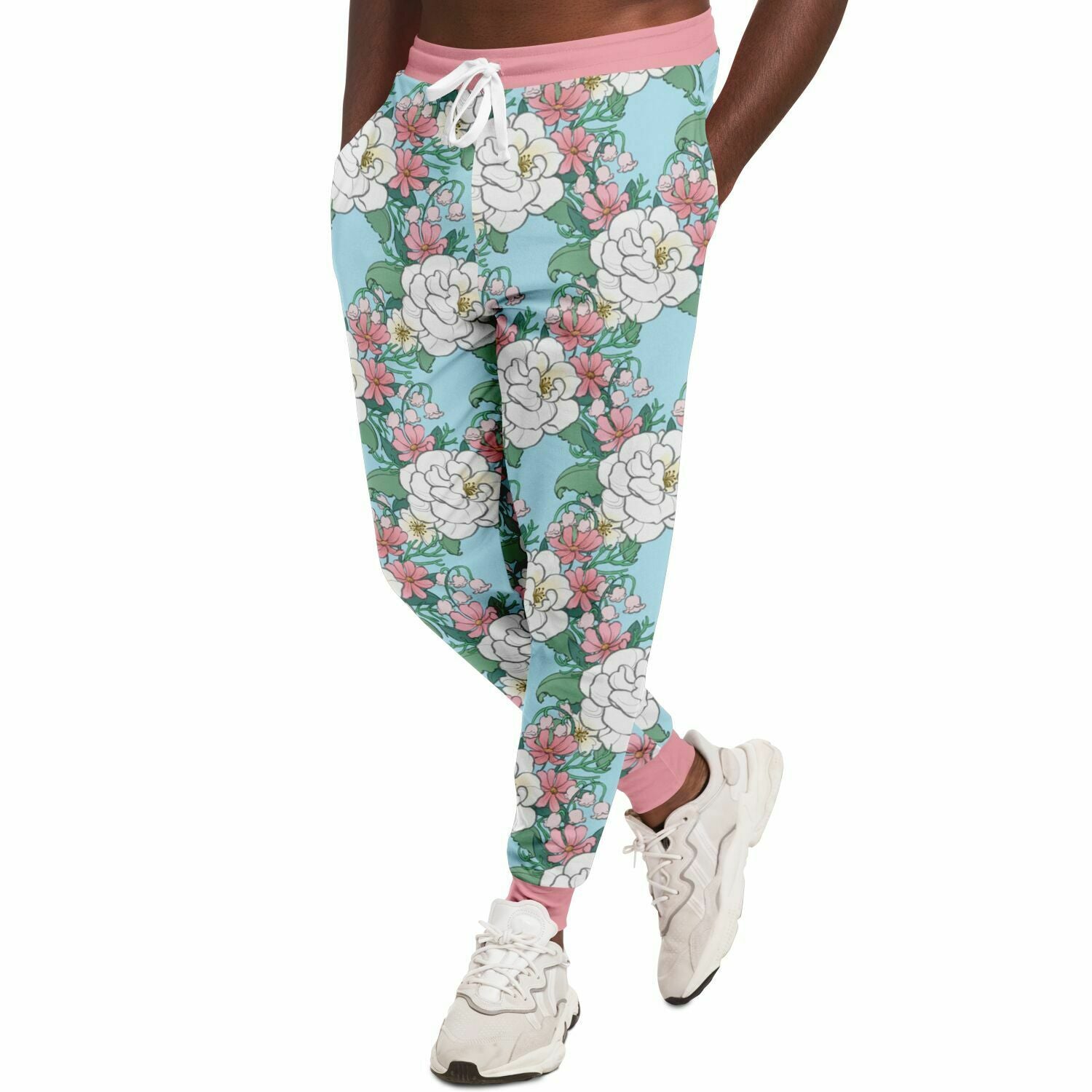 A model wearing a Joggers. The jogger's pattern features white wild roses, pink cosmos, and lillies of the valley on a light blue background. it has a pink hem and cuffs.